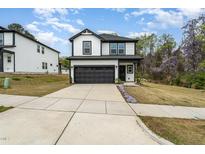 Two-story home featuring a black garage door, concrete driveway, black trim, and small patches of purple flowers at 304 Diversity Way, Raleigh, NC 27610