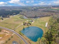 Expansive aerial view of a farmhouse featuring a large pond, pastures, and wooded areas creating a serene country estate at 97 Bailey Rd, Coats, NC 27521