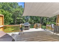 A wooden deck with a grill, patio furniture, and a shade cover, surrounded by lush greenery at 2832 Steeple Run Dr, Wake Forest, NC 27587