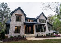 Stunning stone home with black trim, complemented by lush landscaping at 2200 Paddstowe Main Way, Wake Forest, NC 27587