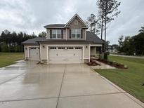 New two-story home showcasing a three-car garage, neutral siding, and professionally landscaped front yard on a cloudy day at 18 Bonnybrook Ct, Selma, NC 27576