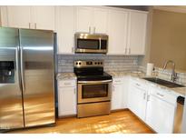 Bright kitchen with stainless steel appliances, white cabinets, stone countertops, and a stylish subway tile backsplash at 108 W Savannah Ridge Rd, Holly Springs, NC 27540