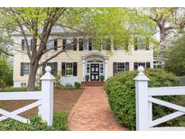 Charming two-story home with yellow siding, black shutters, brick walkway, and a white picket fence at 1208 College Pl, Raleigh, NC 27605