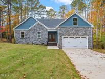Charming home boasts a stone facade, blue accents, an attached two-car garage, and a well-manicured lawn at 42 Ponchartrain St, Fuquay Varina, NC 27526