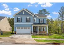 Charming two-story home with blue siding, a covered porch, and a two-car garage in a lush landscape at 5209 Woodlawn Dr, Durham, NC 27703