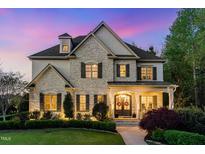 Charming stone home with a manicured lawn and inviting entrance at twilight at 104 Vervain Way, Holly Springs, NC 27540