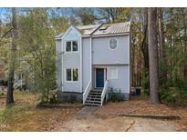 Charming two-story home featuring a blue front door, unique windows, and a metal roof surrounded by a wooded area at 19 Lansgate Ct, Durham, NC 27713