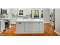 Bright kitchen with a large island, stainless steel appliances, blue tile backsplash and white cabinets at 6216 Valley Estates Dr, Raleigh, NC 27612