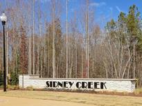 Welcoming Sidney Creek community sign with manicured landscaping, set against a backdrop of trees and a bright blue sky at 1017 Channel Drop Lp, Zebulon, NC 27597