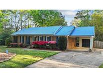 Charming brick home with a striking blue metal roof, lush landscaping, and a convenient carport at 801 Silver Leaf Pl, Raleigh, NC 27609