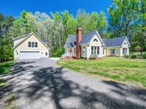 Charming yellow home featuring a brick chimney, a garage, and a well-maintained lawn and gravel driveway at 1208 Goodwin Rd, Apex, NC 27523