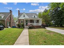 Charming brick home boasts a cozy front porch and beautifully landscaped front yard under a bright, cloudy sky at 1105 Englewood Ave, Durham, NC 27701