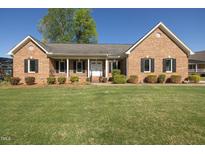 Charming brick home featuring a well-manicured lawn, covered front porch, and mature landscaping at 627 Carraway Dr, Graham, NC 27253