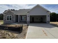 New construction featuring a two-car garage, stone accents and gray vinyl siding, with an unfinished yard at 69 Tee Dr, Selma, NC 27576