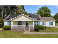 Charming single-story home features a covered front porch, bright blue shutters, solar panels, and a well-manicured lawn at 10 Gray Bass Ct, Zebulon, NC 27597