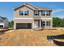 New two-story home showcasing a two-car garage, tan siding, dark shutters, and a white front door at 84 Grove Township Way, Angier, NC 27501