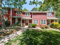 Charming red townhome featuring a well-manicured lawn, inviting front porch, and lush landscaping at 116 Old Maple Ln, Durham, NC 27713