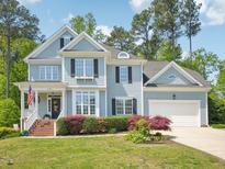 Charming two-story home with light-blue siding, black shutters, manicured landscaping, and an attached garage at 5708 Butter Churn Way, Fuquay Varina, NC 27526