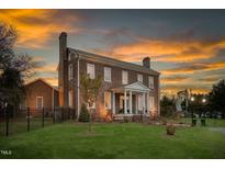 Stately brick home featuring a columned front porch and lush green lawn under a colorful sky at 3542 Bason Rd, Mebane, NC 27302