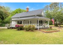 Charming two-story white home with a welcoming wraparound porch, vibrant landscaping, and an American flag at 119 Johnson St, Broadway, NC 27505