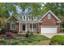 Charming brick home featuring a welcoming front porch, attached garage, and lush landscaping at 103 Temple Gate Dr, Cary, NC 27518