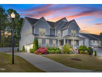 Beautiful two-story home featuring a welcoming front porch and lush landscaping at sunset at 3037 Freeman Farm Way, Rolesville, NC 27571