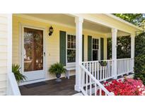 Inviting front porch with wood decking, red azaleas, white railings and posts, and yellow siding at 1140 Buttercup Ln, Wake Forest, NC 27587