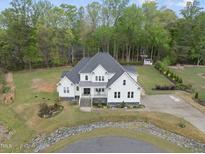 Stunning aerial view of a white home with a gray roof, landscaping, and a spacious yard surrounded by lush trees at 6024 Lunenburg Dr, Raleigh, NC 27603