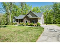 Inviting single-story home featuring stone accents, well-maintained landscaping, and a paved driveway on a sunny day at 4057 Mackenzie Dr, Haw River, NC 27258