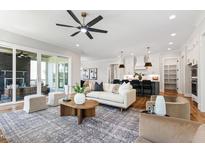 Open concept living room featuring a ceiling fan, hardwood floors, a modern sofa, and a view into the kitchen at 928 Lily Claire Ln, Fuquay Varina, NC 27526