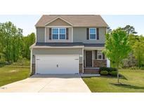 Two-story home features a two-car garage, neutral siding, and a well-maintained front yard with new tree at 80 Doonbeg Dr, Fuquay Varina, NC 27526