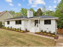 Charming white brick home with a landscaped yard, inviting front porch, and a classic chimney at 1310 Mayfair Rd, Raleigh, NC 27608