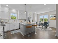 Bright kitchen featuring white cabinets, stainless steel appliances, island with bar stools, and adjacent dining area at 241 Connelly Way, Zebulon, NC 27597