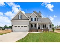 Charming two-story home with a well-manicured lawn and a two-car garage under a sunny, partly cloudy sky at 186 Gumtop Dr, Zebulon, NC 27597