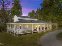 Stunning exterior of a home with a wraparound porch and a metal roof surrounded by mature trees at 9400 Wheelers Church E Rd, Hurdle Mills, NC 27541