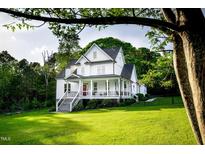 Stunning white farmhouse with a covered porch, rocking chairs, and a well-manicured front lawn at 1023 Laura Johnson Rd, Pittsboro, NC 27312