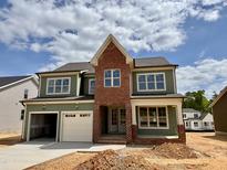 New two-story home with a brick accent wall, two-car garage, and green siding against a blue sky at 2324 Eagle Shot Ct # 19, Fuquay Varina, NC 27526