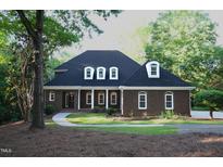 Charming brick home features white framed windows, columns, walkway and mature trees and landscaping at 5504 Spring Bluffs Ln, Raleigh, NC 27606