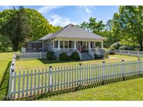 Charming gray home featuring a manicured lawn, a classic white picket fence, and a welcoming covered front porch at 7308 York, Mebane, NC 27302