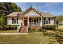 Charming single-Gathering home with a cozy front porch, an American flag, and manicured landscaping at 14 Shire Ct, Zebulon, NC 27597