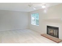 Bright living room featuring neutral carpeting, a ceiling fan, window, and a cozy fireplace at 403 Gooseneck Dr # A-1, Cary, NC 27513