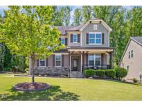 Inviting two-story home featuring a landscaped front yard and a charming covered porch with stone accents at 1557 Tice Hurst Ln, Apex, NC 27502