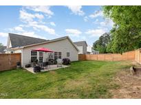 Well-maintained backyard featuring a patio with outdoor seating, a fire pit, and a spacious grassy area with a wooden fence at 205 Braxcarr St, Holly Springs, NC 27540