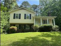 Two-story home with yellow siding, brick foundation, covered front porch, and manicured lawn surrounded by lush greenery at 7412 Barberry Ct, Raleigh, NC 27615