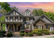 Charming two-story home with a stone facade, covered porch, and manicured landscaping under a colorful sunset at 2821 Penfold Ln, Wake Forest, NC 27587