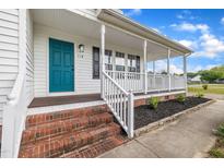 Charming front porch featuring a teal door, white columns, and brick steps at 112 Edmondson Dr, Willow Springs, NC 27592