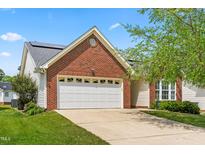 Charming brick home featuring an attached garage, well-manicured lawn, and solar panels on the roof at 210 Millet Dr, Morrisville, NC 27560
