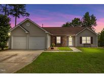 Charming single-story home featuring a well-manicured lawn, two-car garage, and lovely facade at twilight at 308 Holly Briar Dr, Fuquay Varina, NC 27526