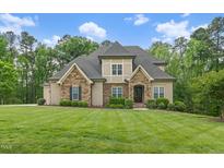 Beautiful stone and siding home with manicured lawn and mature trees on a sunny day at 325 Forest Bridge Rd, Youngsville, NC 27596
