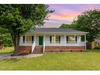Charming single-story home with a welcoming front porch and manicured lawn at sunset at 5317 Cottage Bluff Ln, Knightdale, NC 27545